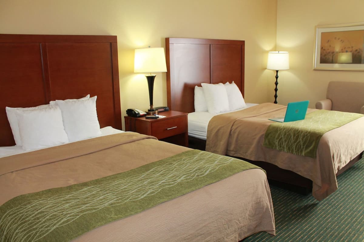 A hotel room with two beds, a desk, a chair, a laptop, and a lamp.
