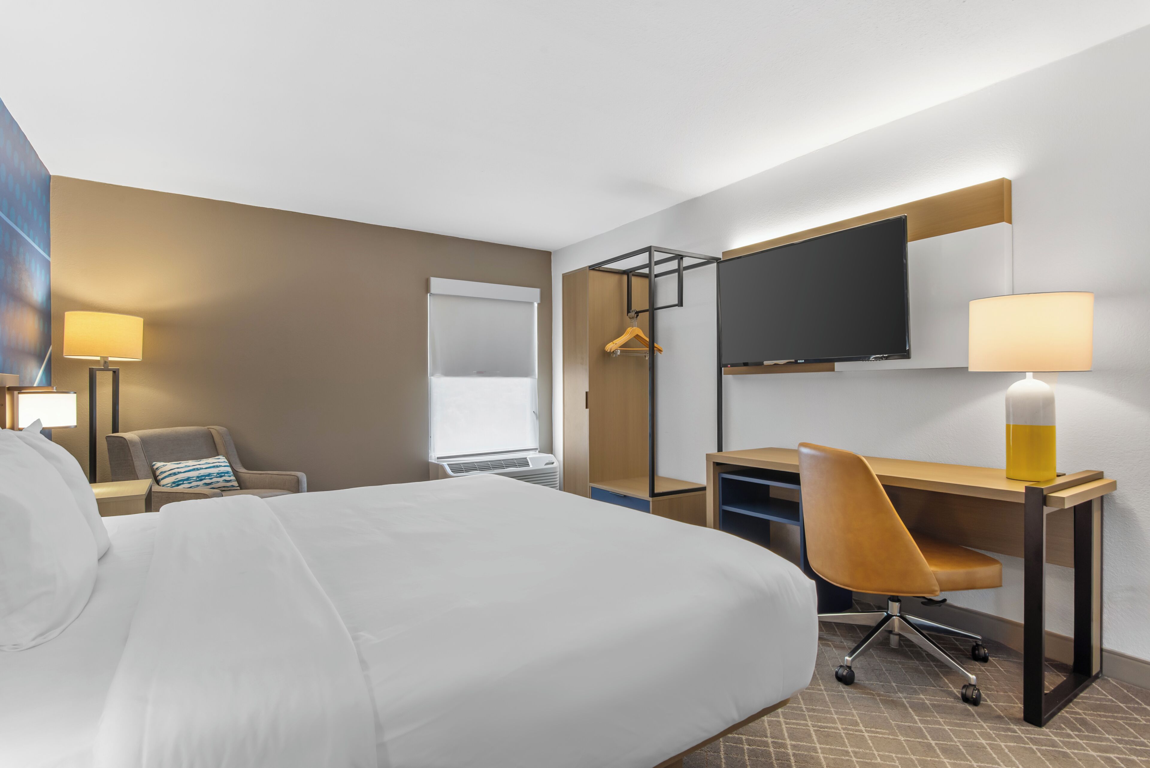 Una habitación de hotel con cama, escritorio, silla, televisor y lámpara.