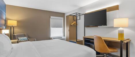 Una habitación de hotel con cama, escritorio, silla, televisor y lámpara.