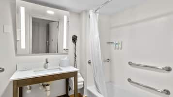 Une salle de bain avec un lavabo blanc, un miroir et une douche équipée de barres d’appui.