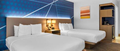 A hotel room with two beds, a wall with a blue dot pattern, a painting, and a built-in shelf.