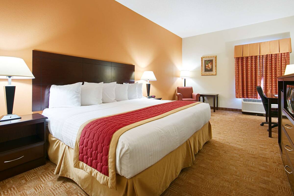 A hotel room with a large bed, two bedside lamps, a television, a chair, and a small table.
