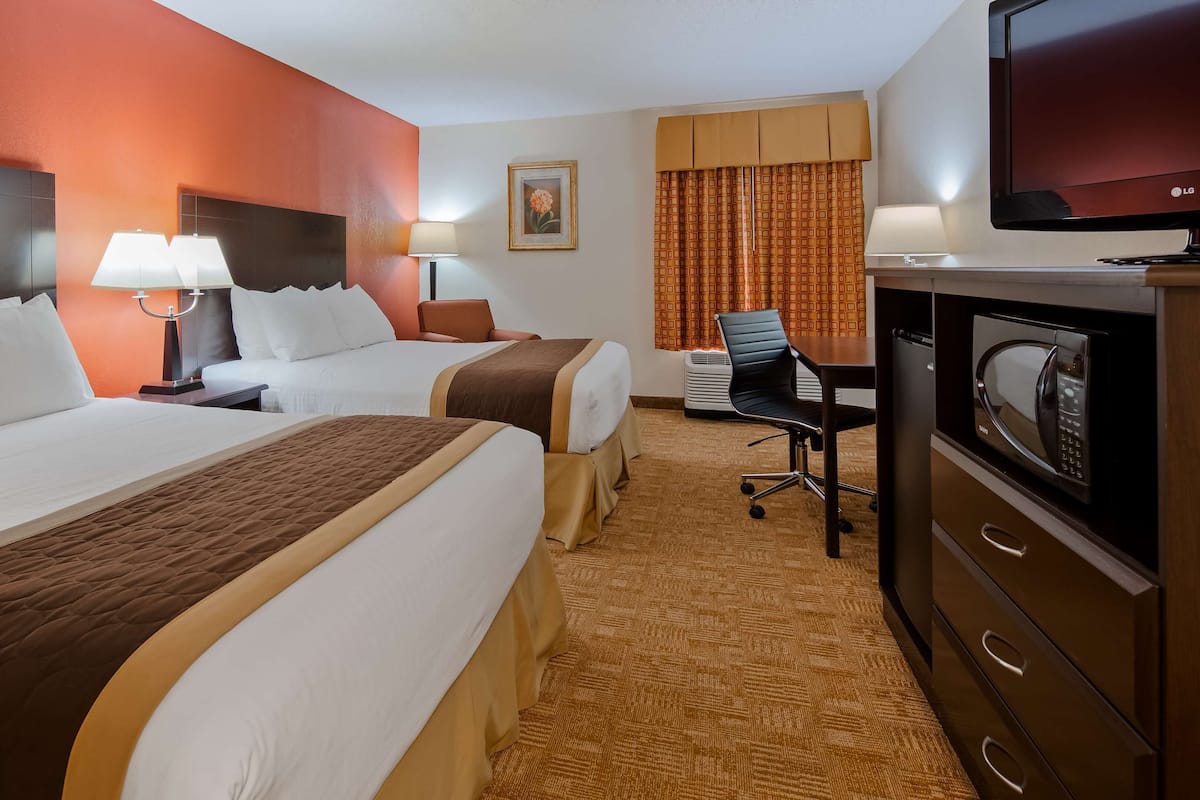 A hotel room with two beds, a desk with a computer, a TV, and a microwave.