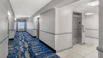 Un pasillo de hotel con alfombra azul estampada, paredes blancas y un ascensor.