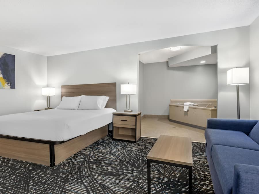 Une chambre d’hôtel comprenant un lit, des tables de chevet, un bureau, une chaise, une salle de bain et un grand miroir.