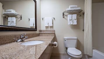 A bathroom with a granite countertop sink, a mirror, a toilet, and towel racks.