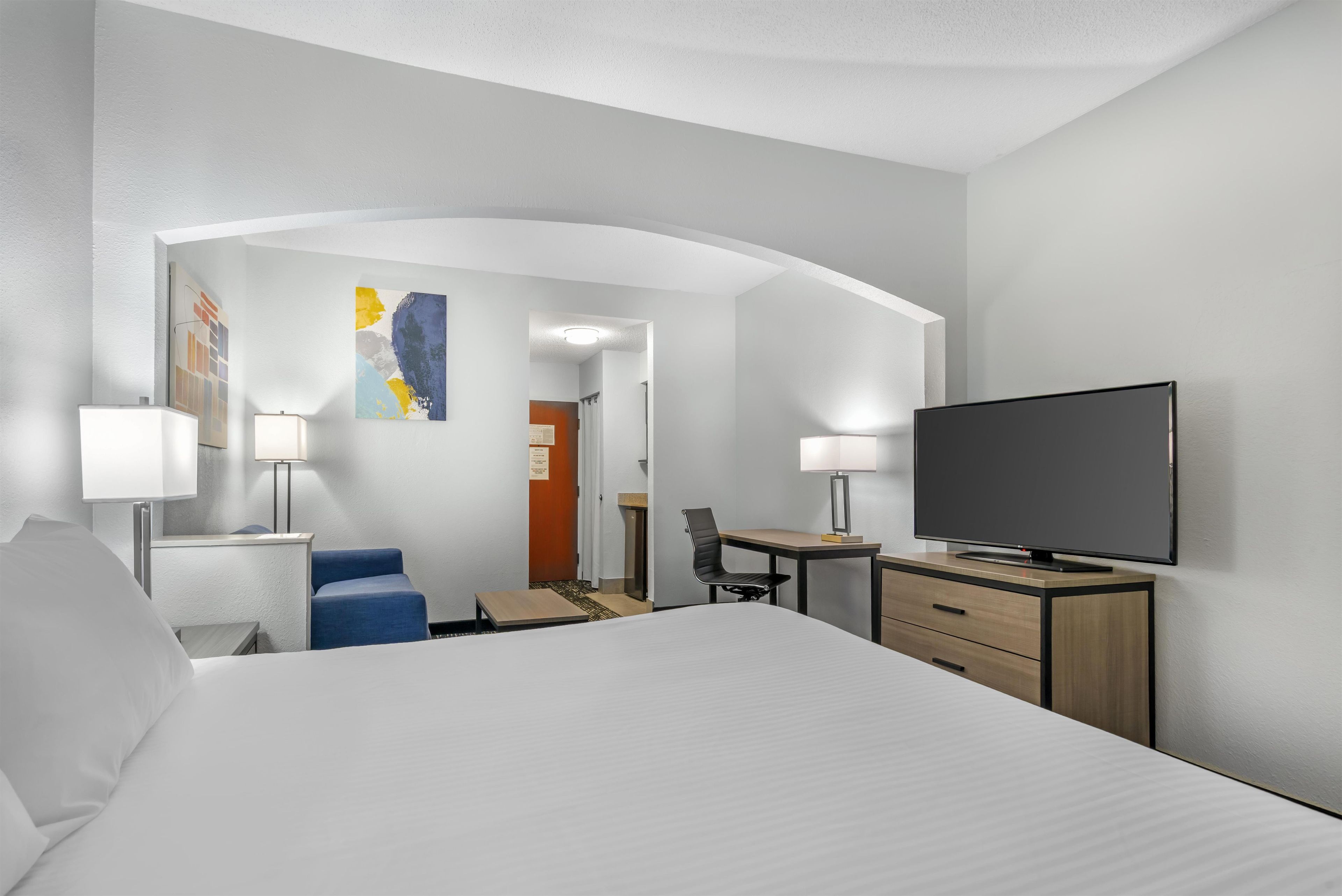 Habitación de hotel con cama, escritorio, silla, televisor y lámparas.