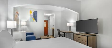 Habitación de hotel con cama, escritorio, silla, televisor y lámparas.