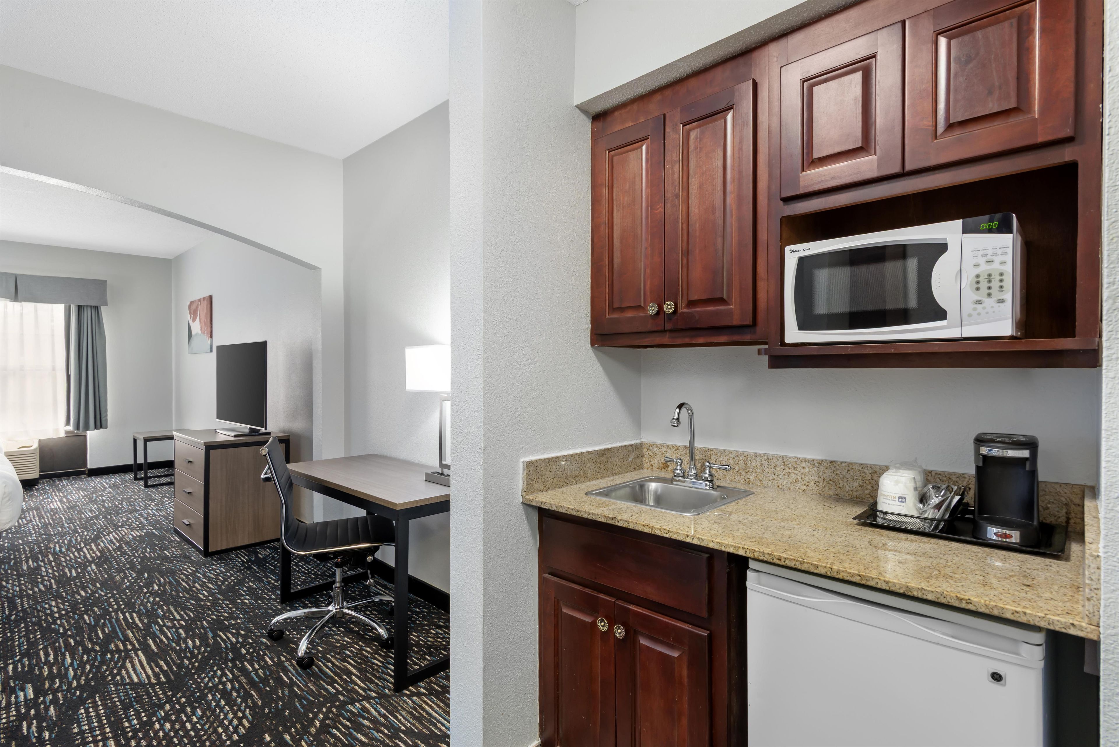 Una habitación de hotel con escritorio, silla, kitchenette y cama.
