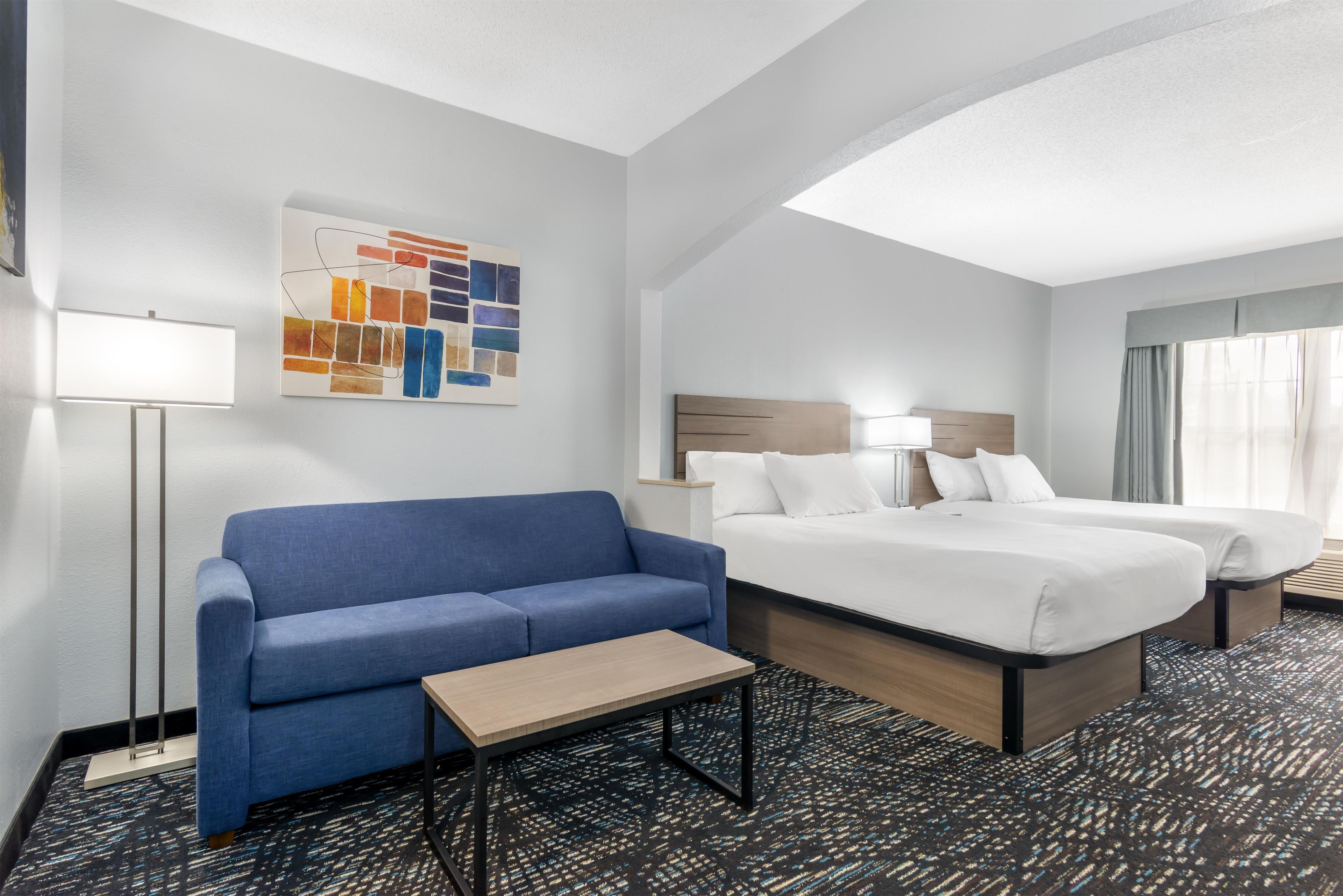 Ein Hotelzimmer mit Bett, einer Couch, einem kleinen Tisch, einer Lampe und einem Wandbild.