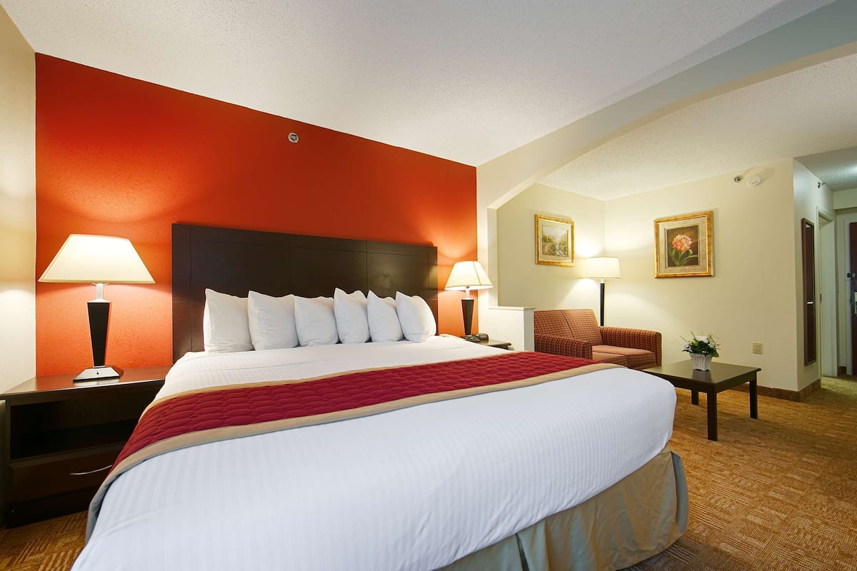 A hotel room with a large bed, two bedside tables with lamps, a chair, and two framed pictures on the wall.