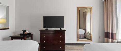 A hotel room with two beds, a dresser, a flat-screen TV, and a mirror reflecting the room.