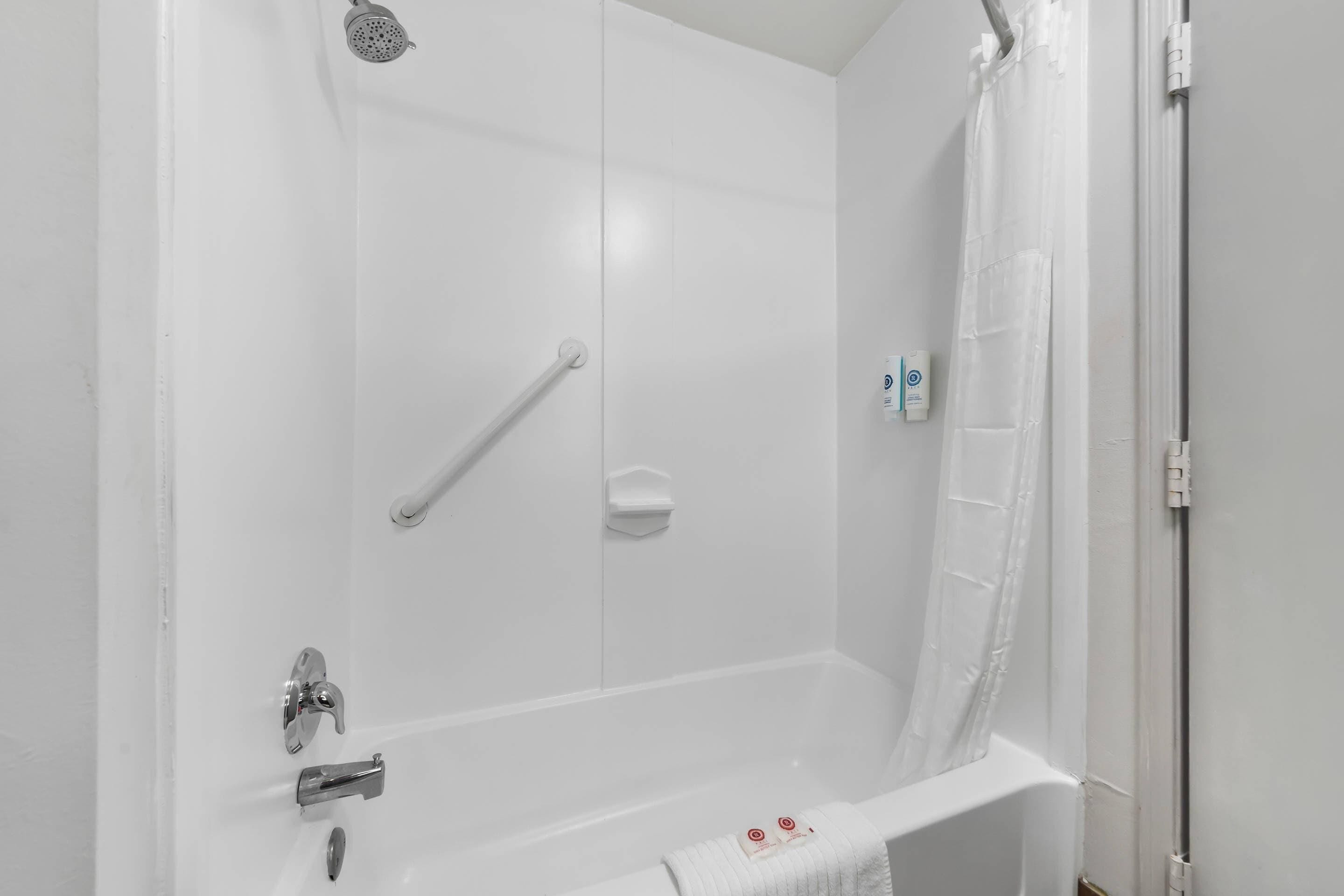 A white bathtub with a showerhead, grab bar, and a towel rack.