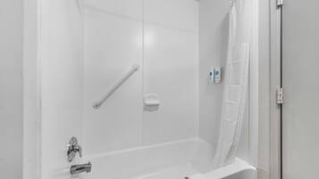 Una bañera blanca con cabezal de ducha, barra de apoyo y toallero.