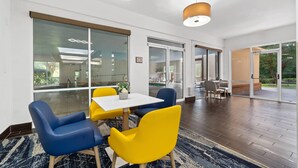 Ein moderner Konferenzraum mit einem weißen Tisch, blau-gelben Stühlen und großen Fenstern mit Blick ins Freie.