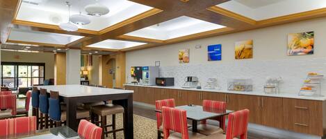 Un vestíbulo de hotel con un comedor central, una estación de café y obras de arte en las paredes.