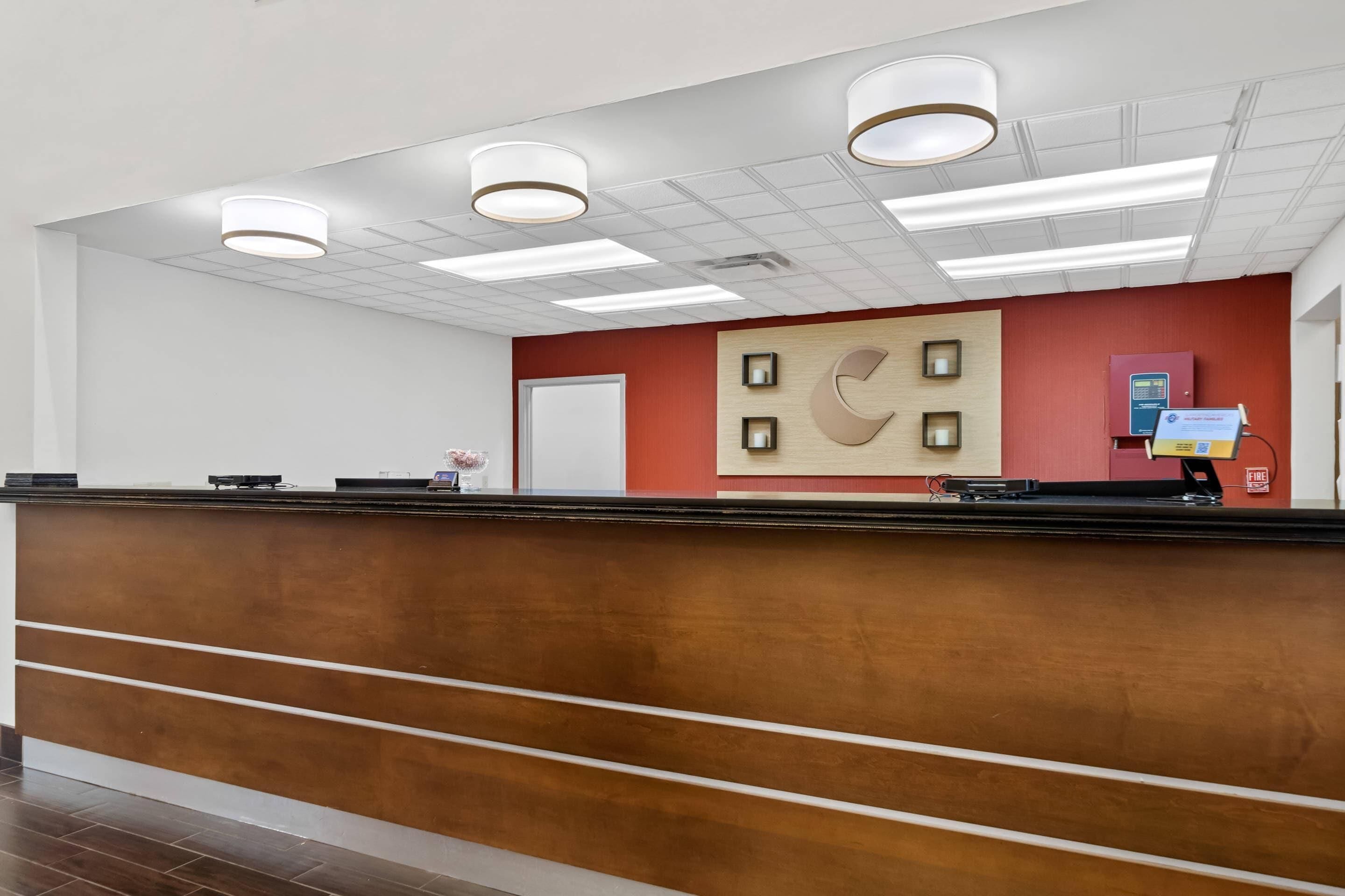Un área de recepción con un mostrador de madera, una puerta blanca y un quiosco informativo adosado a la pared.