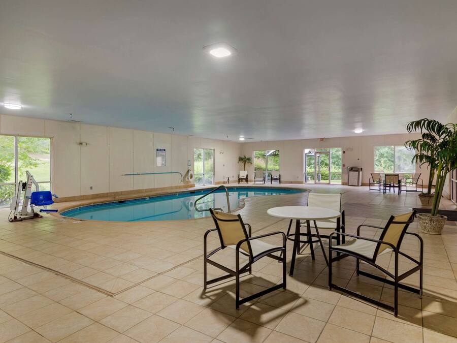 A spacious indoor swimming pool area with a pool table and chairs, large windows, and a ceiling fan.