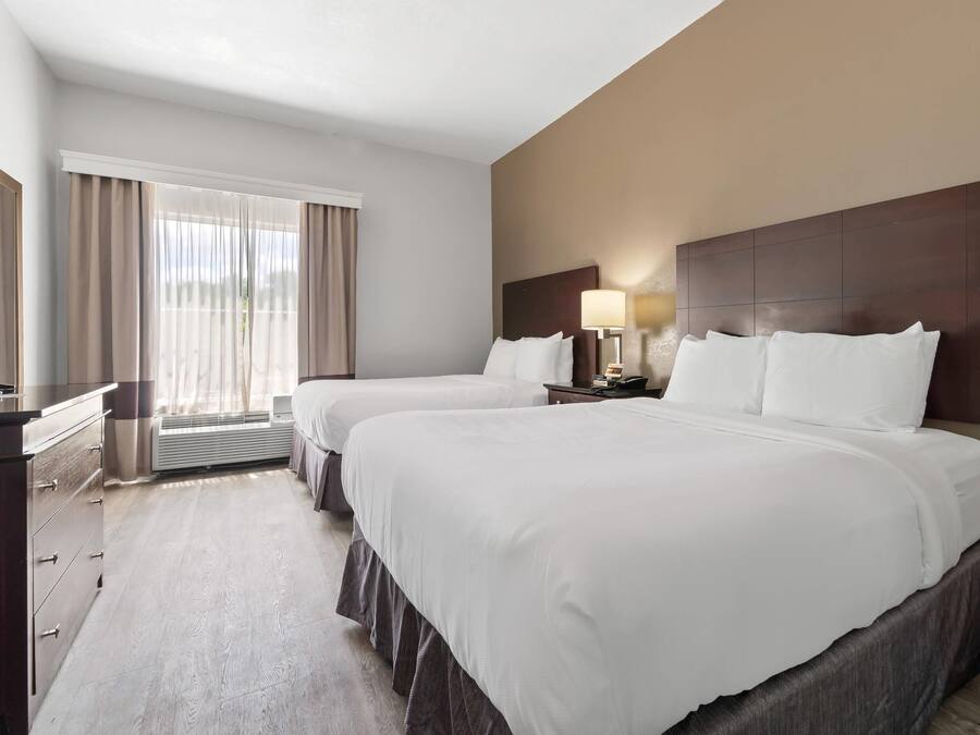 A hotel room with two beds, a desk, a television, and a window with curtains.