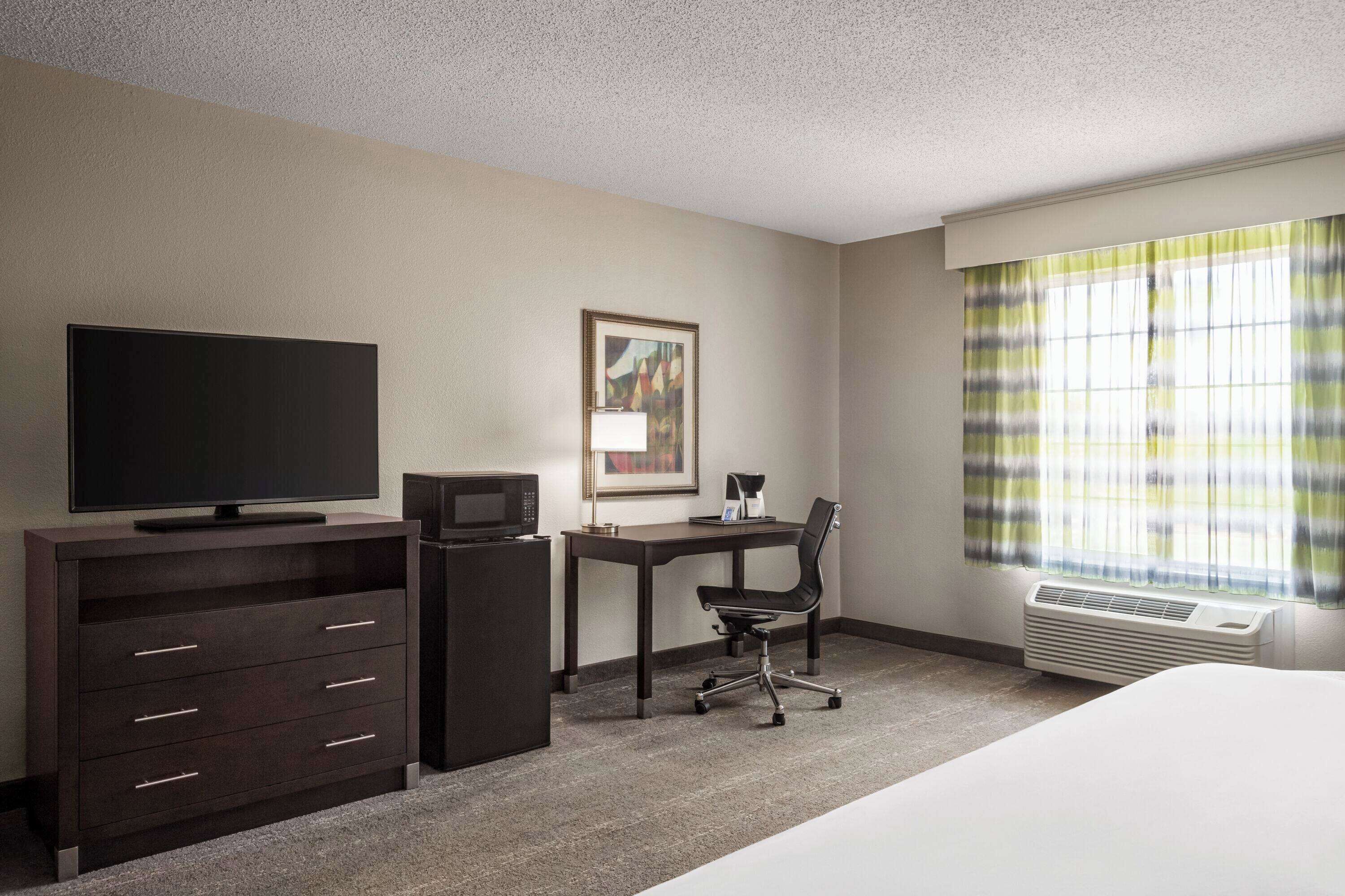 A hotel room with a bed, a desk with a chair, a television, a microwave, and a framed picture on the wall.