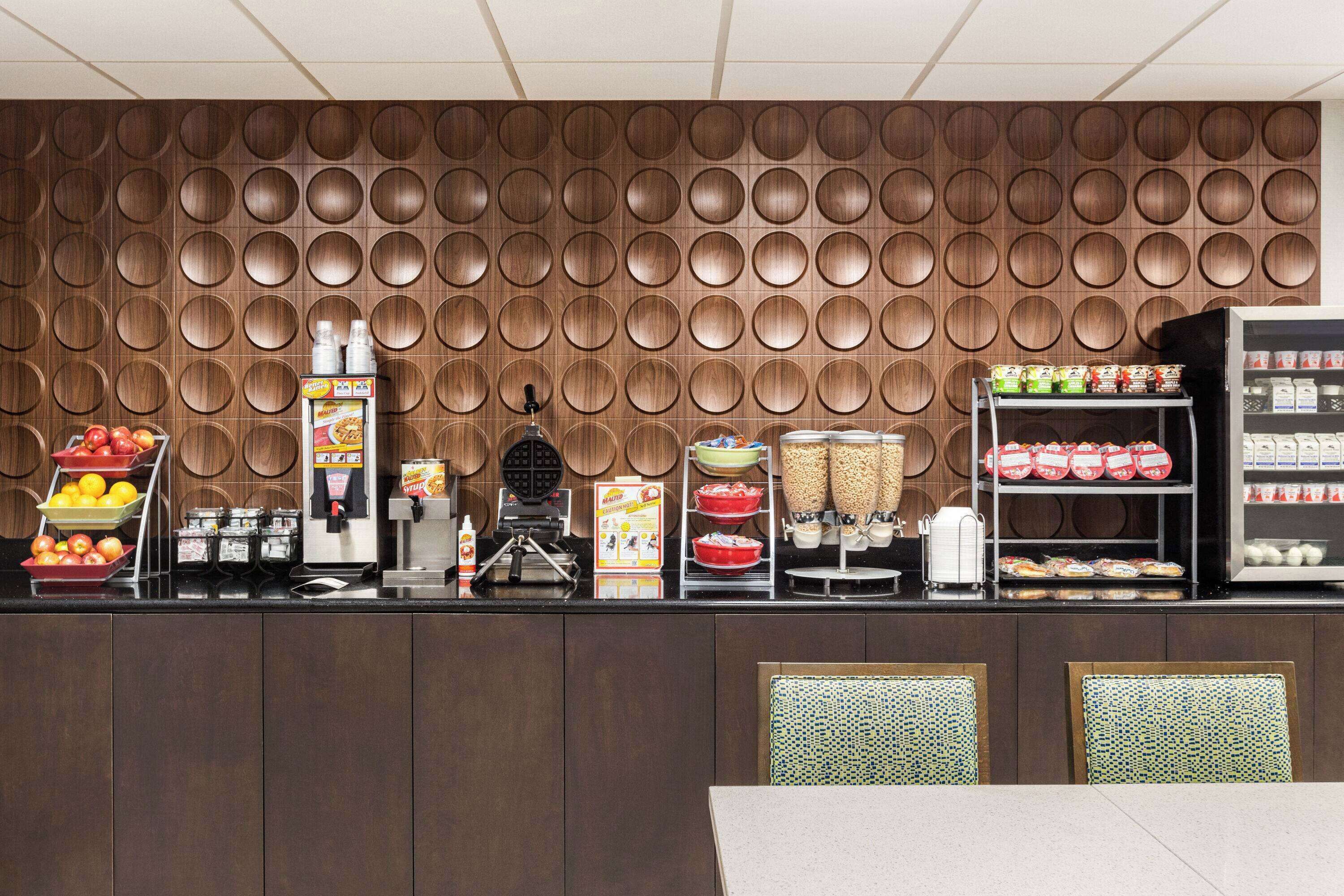 A breakfast bar with a variety of food items and beverages, including fruits, cereals, and packaged goods.