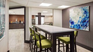 Una sala de conferencias con una larga mesa y sillas verdes, un cuadro abstracto grande en la pared y una zona de cocina al fondo.