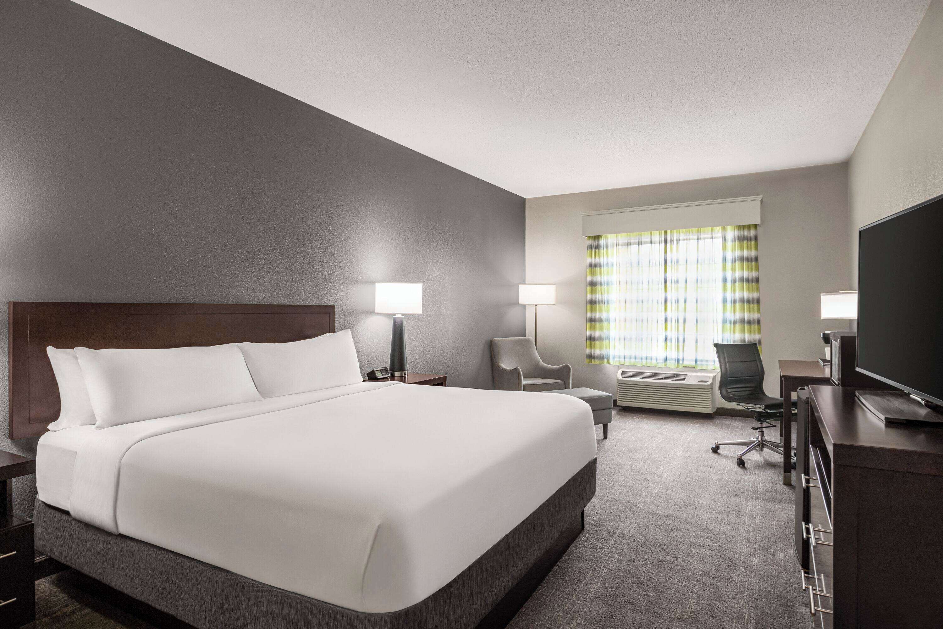 A hotel room with a large bed, two bedside tables, a desk with a chair, a television, and a window with curtains.