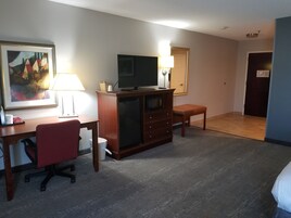 Habitación de hotel con escritorio, silla, televisor, cómoda y un pequeño banco.