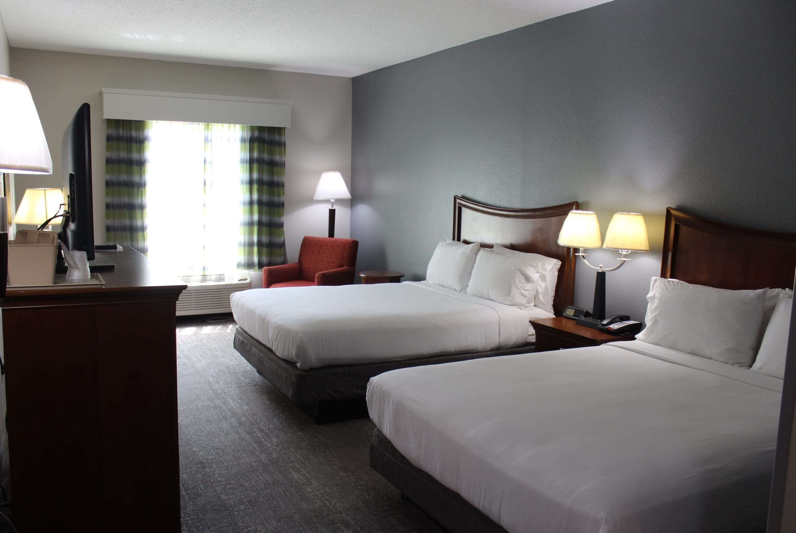 Quarto de hotel com duas camas, uma mesa, uma cadeira e uma janela com cortinas.