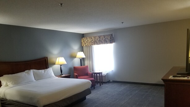 Habitación de hotel con una cama grande, dos lámparas de noche, un sillón rojo, una mesita y una ventana con cortinas.