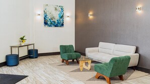 Un espacio lounge moderno con un sofá blanco, dos sillones verdes, una mesita de café y un cuadro en la pared.
