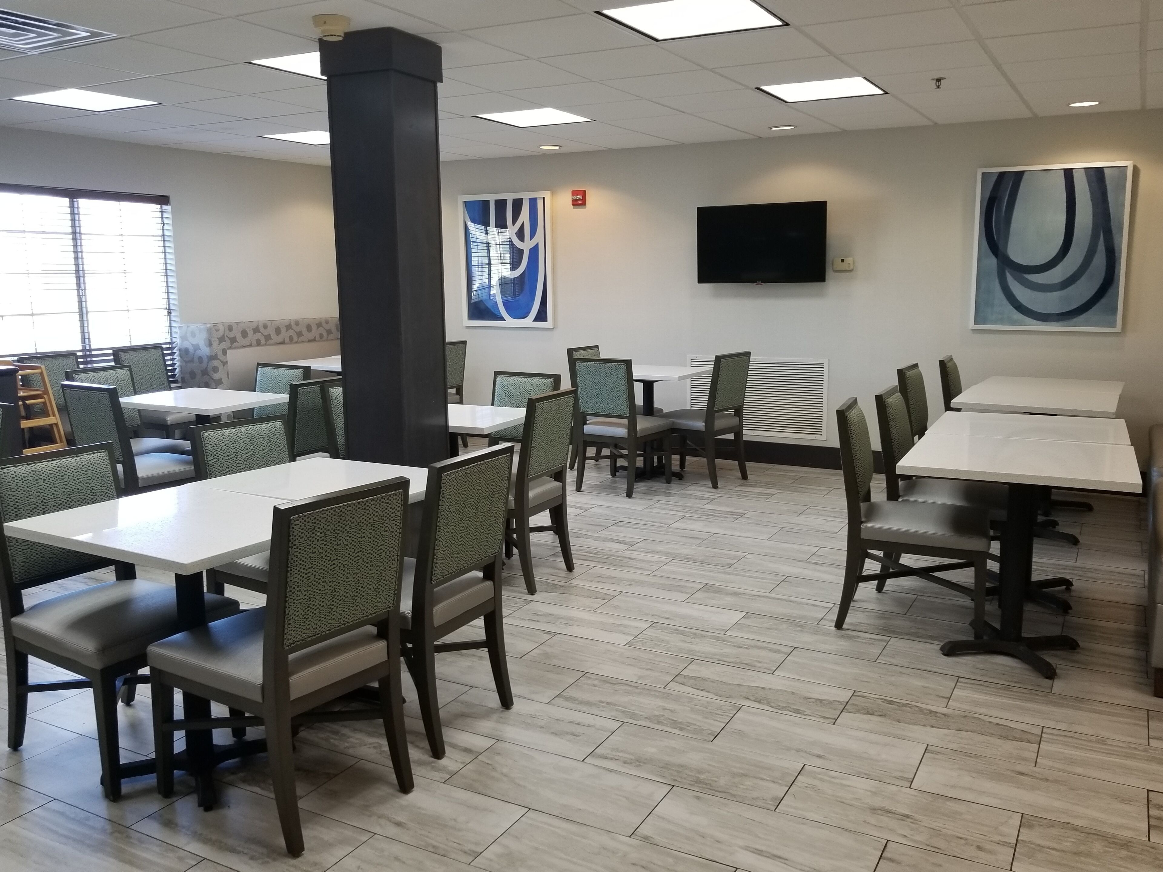 A restaurant with multiple tables and chairs, a large pillar, a flat-screen TV, and artwork on the walls.