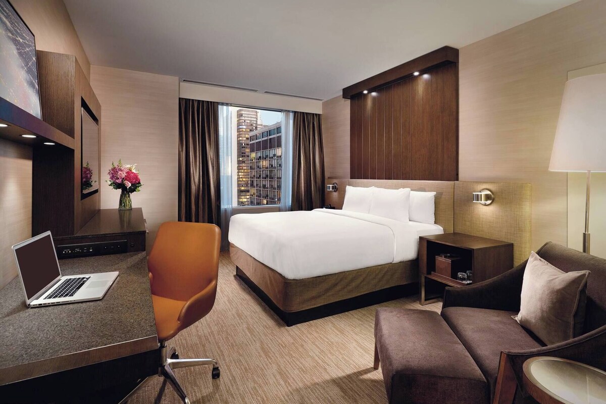 Habitación de hotel con cama, escritorio, silla y vista a la ciudad.