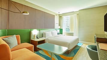 A hotel room with a bed, a green upholstered sofa, a small table, a nightstand with a lamp, and a television.