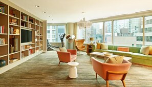 A modern living room with a large bookshelf, a television, and a city view. - Hyatt Centric Chicago Magnificent Mile (Chicago)