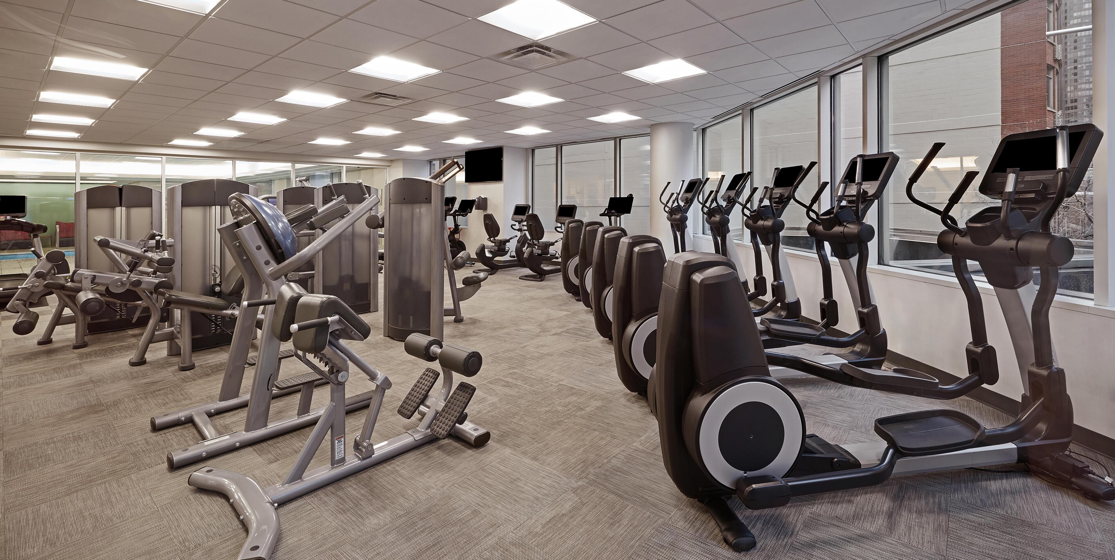 A gym with various exercise equipment, including treadmills and weight machines, arranged in rows.