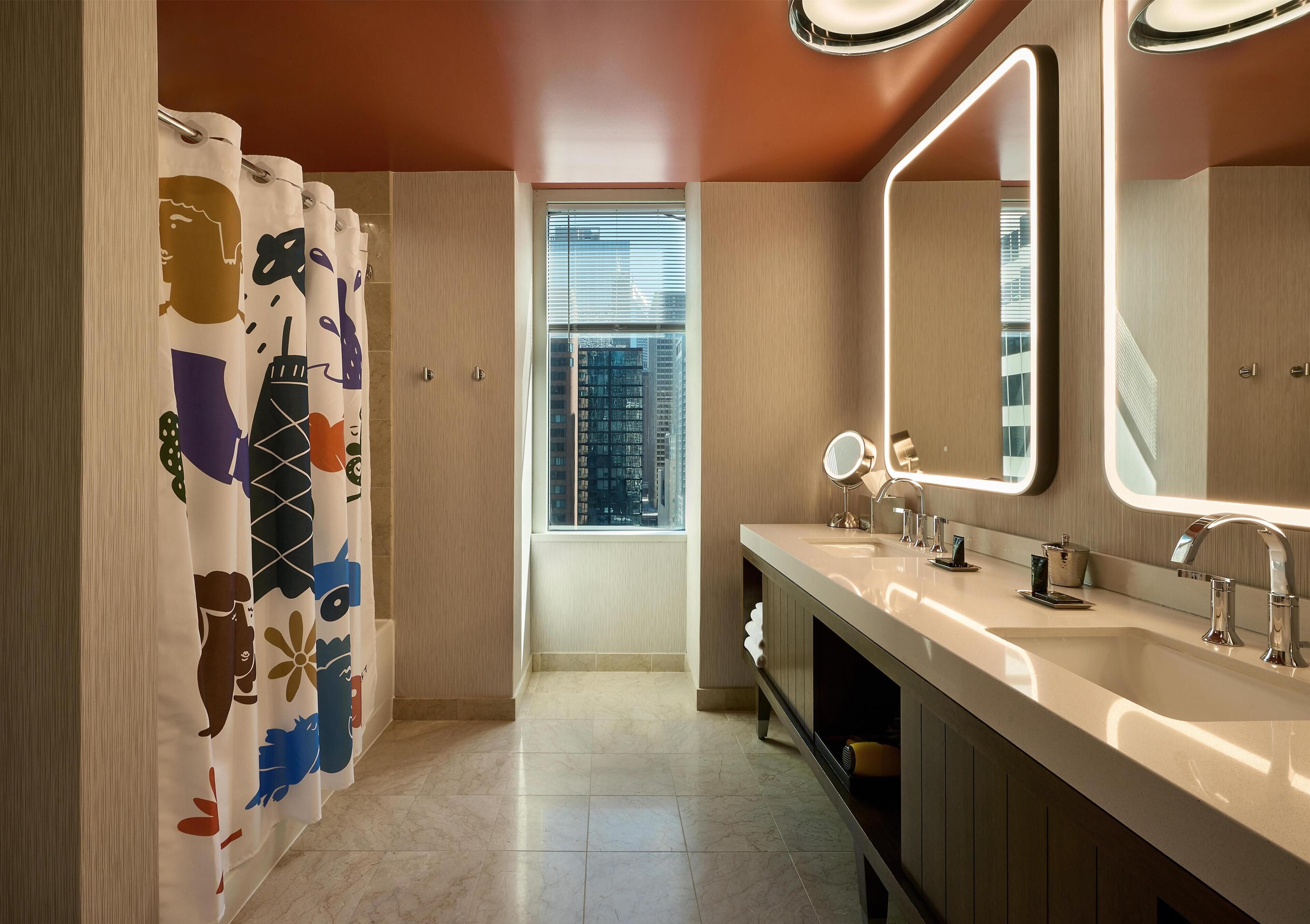 A modern bathroom with a vanity, mirrors, and a window with a city view.