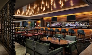 A bar area with multiple seating options, a bar counter with a variety of bottles, and a modern ceiling design. - Hyatt Centric Chicago Magnificent Mile (Chicago)