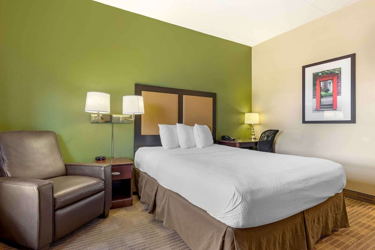 A hotel room with a large bed, a leather chair, two bedside tables with lamps, and a framed picture on the wall.