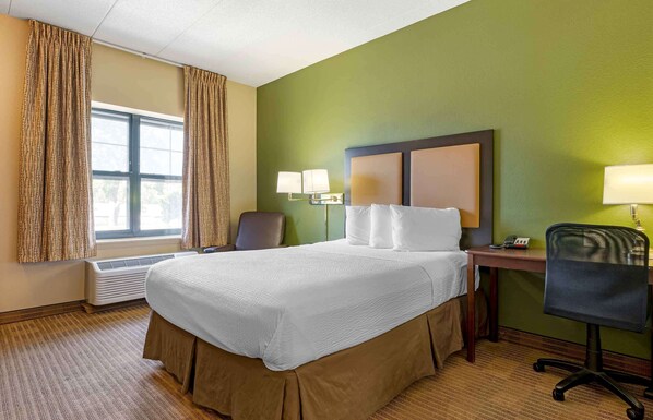 Ein Hotelzimmer mit einem großen Bett, zwei Nachttischlampen, einem Schreibtisch mit Stuhl und einem fenster mit Vorhängen.