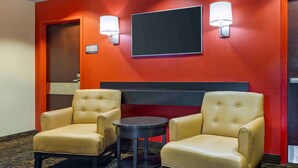 A hotel room with two leather armchairs, a small round table, and a flat-screen TV mounted on the wall. - Extended Stay America Select Suites - Chicago - Darien (Darien)