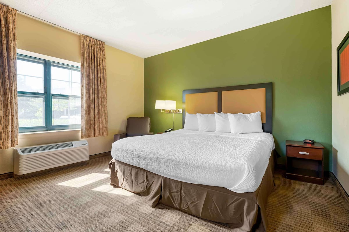 A hotel room with a large bed, a bedside table, a lamp, and a window with curtains.