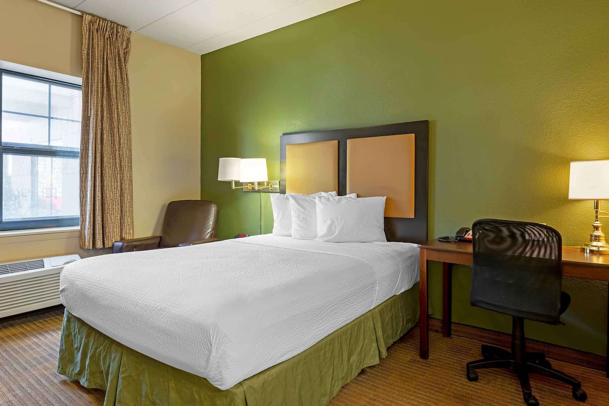 A hotel room with a large bed, two bedside lamps, a desk with a chair, and a window with curtains.