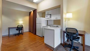 A compact hotel room with a kitchenette, a desk, a chair, a lamp, and a refrigerator. - Extended Stay America Select Suites - Chicago - Darien (Darien)
