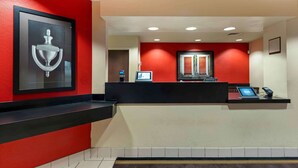 A reception area with a red wall, a black reception desk, a framed door knocker, and a digital display. - Extended Stay America Select Suites - Chicago - Darien (Darien)