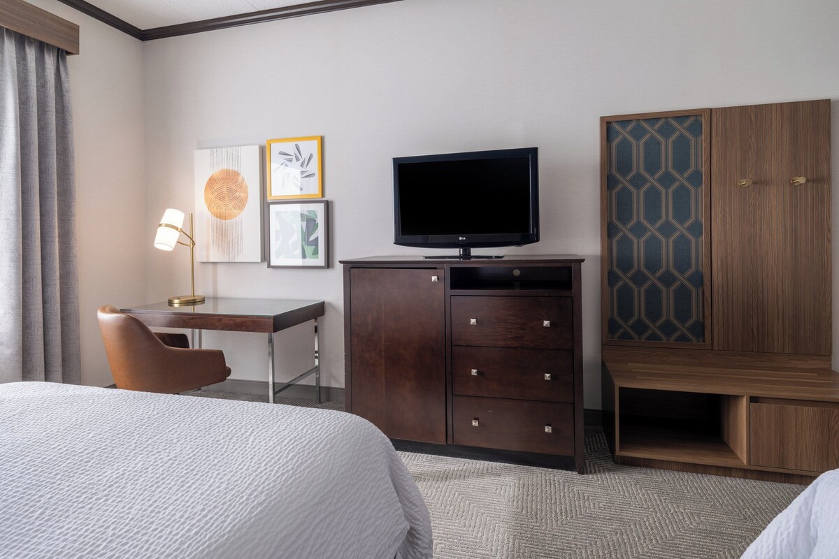 A hotel room with a bed, a desk with a lamp, a television, and a wardrobe.