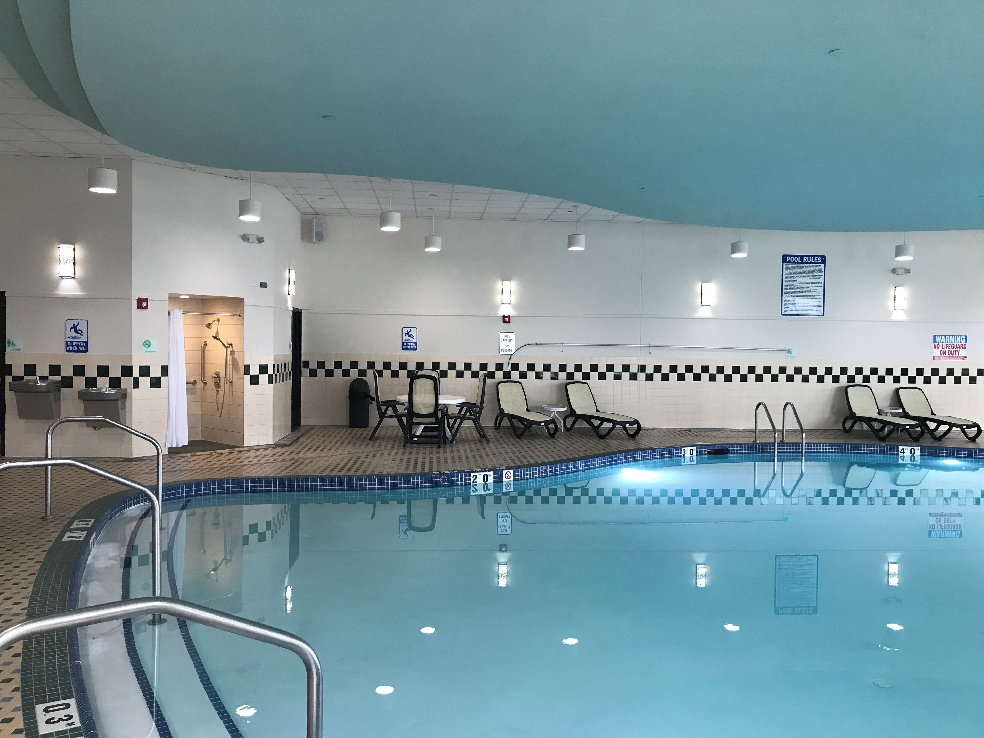 A swimming pool area with lounge chairs, a changing room, and a shower.