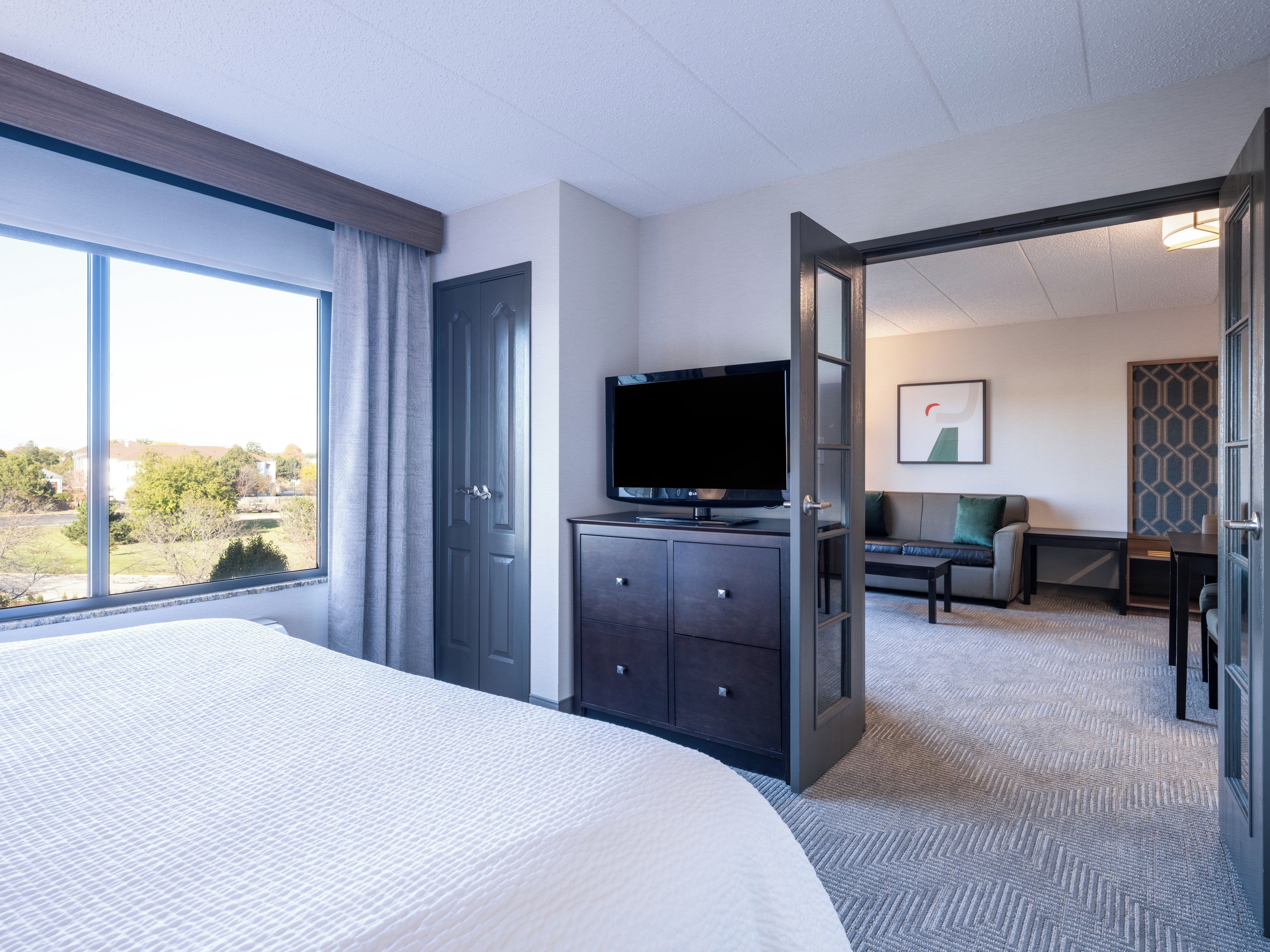 A hotel room with a large bed, a television on a dresser, a sofa, and a view of the outdoors.