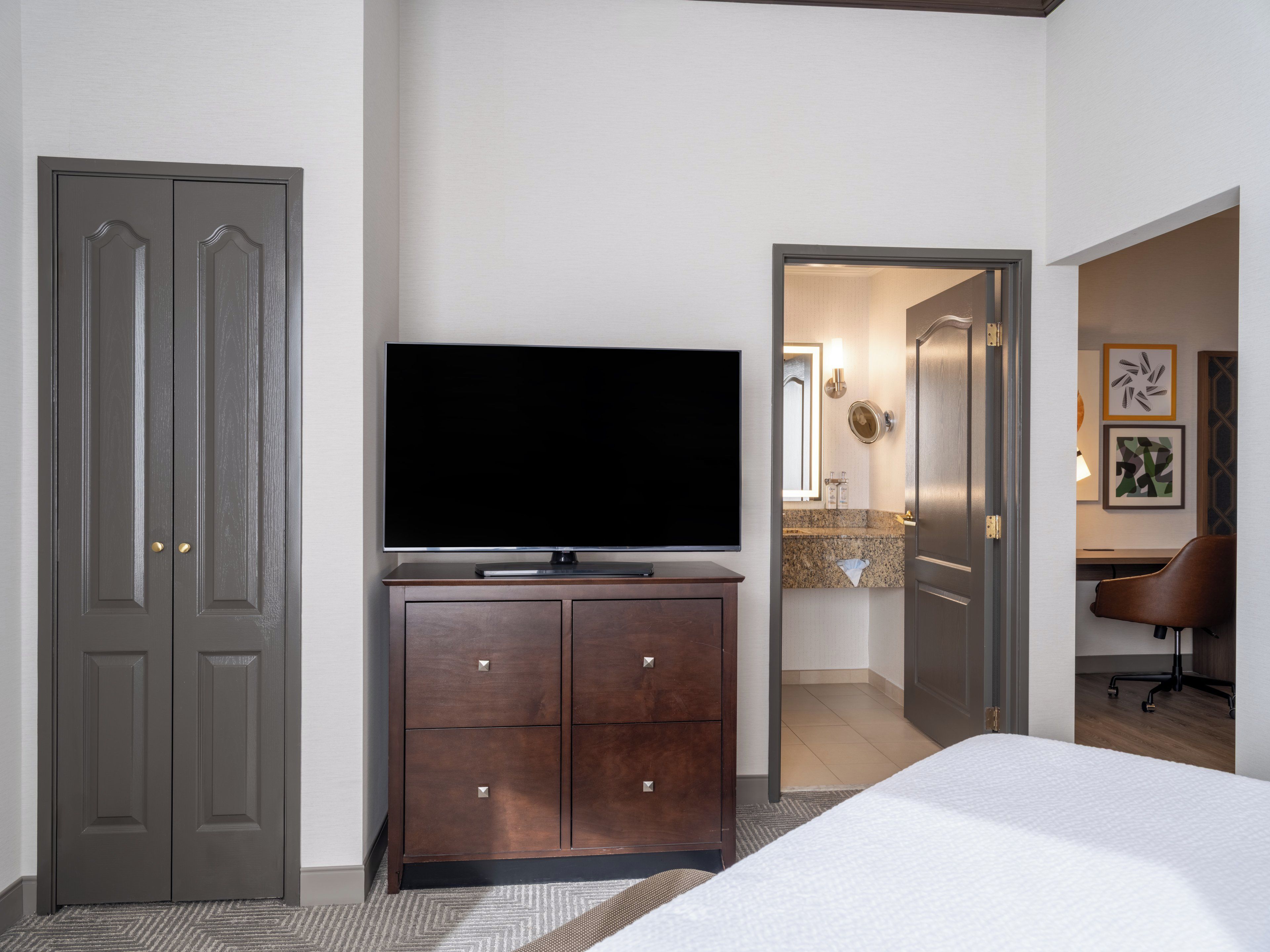 Une chambre d’hôtel équipée d’un lit, d’une télévision, d’une commode et d’un bureau avec une chaise.