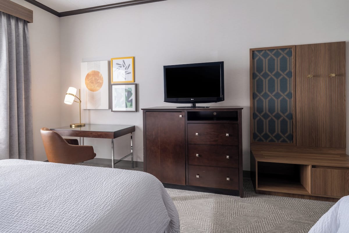 A hotel room with a bed, a desk with a lamp, a television, and a wardrobe.